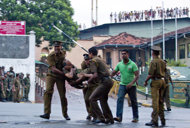 Sri Lankan inmates shout from a roof of a prison building as prison guards carry an injured colleague, foreground right, outside a prison in Colombo, Sri Lanka, Friday, Nov. 9, 2012. Sri Lankan security forces engaged in a gunbattle Friday night with rioting prisoners who appeared to have briefly taken control of at least part of a prison in Colombo. Officials said at least 13 people were wounded in the violence, with several deaths. (AP Photo/Gemunu Amarasinghe)