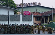 Sri Lankan inmates shout from a roof of a prison building as prison guards assist an injured colleague, foreground right, outside a prison in Colombo, Sri Lanka, Friday, Nov. 9, 2012. Sri Lankan security forces engaged in a gunbattle Friday night with rioting prisoners who appeared to have briefly taken control of at least part of a prison in Colombo. Officials said at least 13 people were wounded in the violence, with several dead. (AP Photo/Gemunu Amarasinghe)