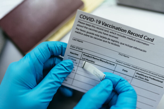 close up hand of doctor put label covid-19 vaccine sticker on vaccination certificate card and passport